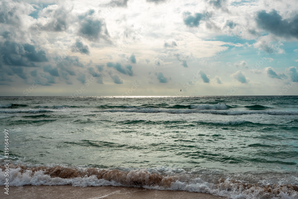 Beautiful Stormy Waves on the coast. Dramatic sky background. Sand beach. Amazing view of grey rainy clouds in the ocean. Sunny rays through the clouds on the horizon. 