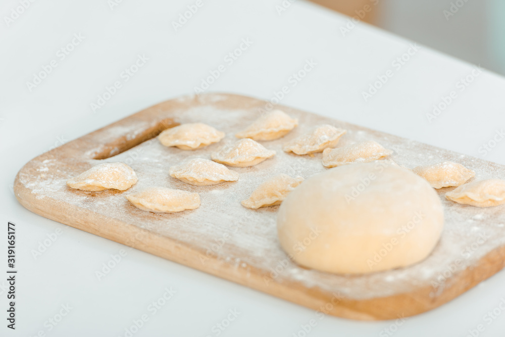 selective focus of flour near raw dumplings on wooden chopping board