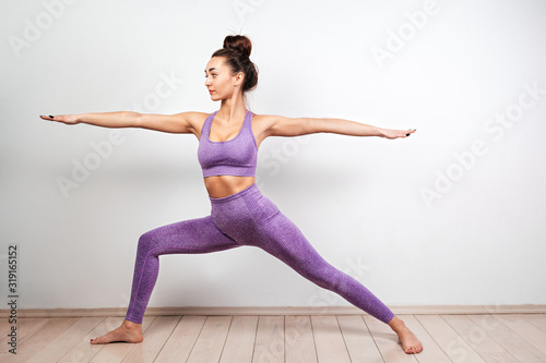 Yoga and sports concept. A young Caucasian woman is engaged in yoga, performing the pose of a warrior. White background in the background. Copy