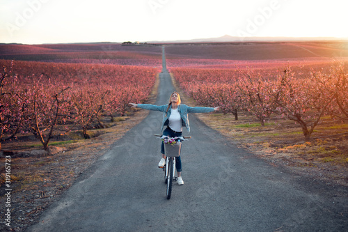 Pretty young woman with a vintage bike enjoying the time in cherry field in springtime. #319165723
