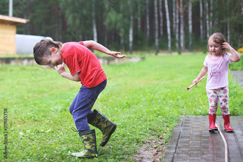 brother and sister play in rainy weather Children jump in puddle and mud in the rain. © stopabox