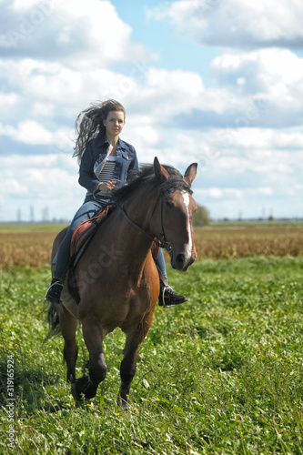 girl in jeans rides a horse in a field in summer