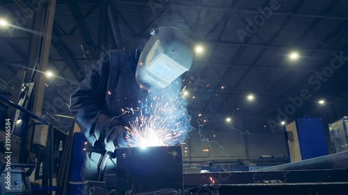 Worker in welder's helmet is welding metal. Slow motion. photo