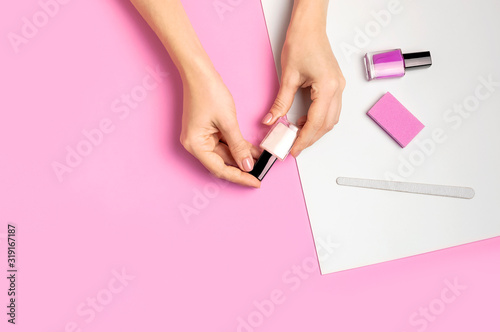 Stylish beautiful gentle manicure. Hands of young woman with nail file  manicure tools on pink background top view flat lay. Natural nails gel polish self-care beauty and fashion. Nail care salon spa