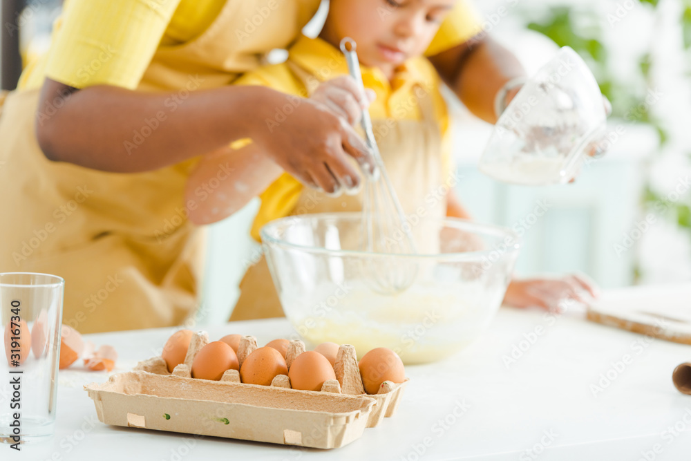 selective focus of eggs near african american kid and mother mixing ingredients in bowl