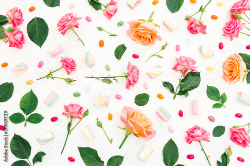 Pattern of roses flowers with candy on white background. Flat lay, top view.