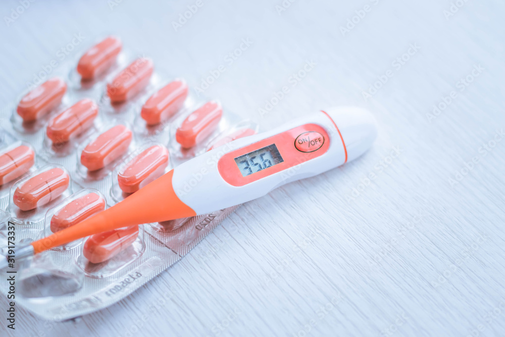 Orange thermometer and pills. Treatment of colds and flu. Body temperature measurement. Normal human body temperature. Tablet vitamins, antiviral drugs and antibiotics. Orange thermometer and pills. Treatment of colds and flu. Body temperature measurement. Normal human body temperature. Tablet vitamins, antiviral drugs and antibiotics.