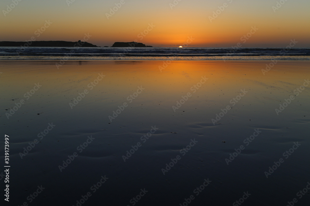 Wet sand at low tide on a sunset background