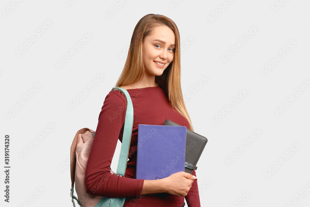 Profile of smiling girl holds leather notebooks in hand and backpack on back. Beautiful young woman isolated on white background in Studio with an empty space for text and advertising. Profile of smiling girl holds leather notebooks in hand and backpack on back. Beautiful young woman isolated on white background in Studio with an empty space for text and advertising.