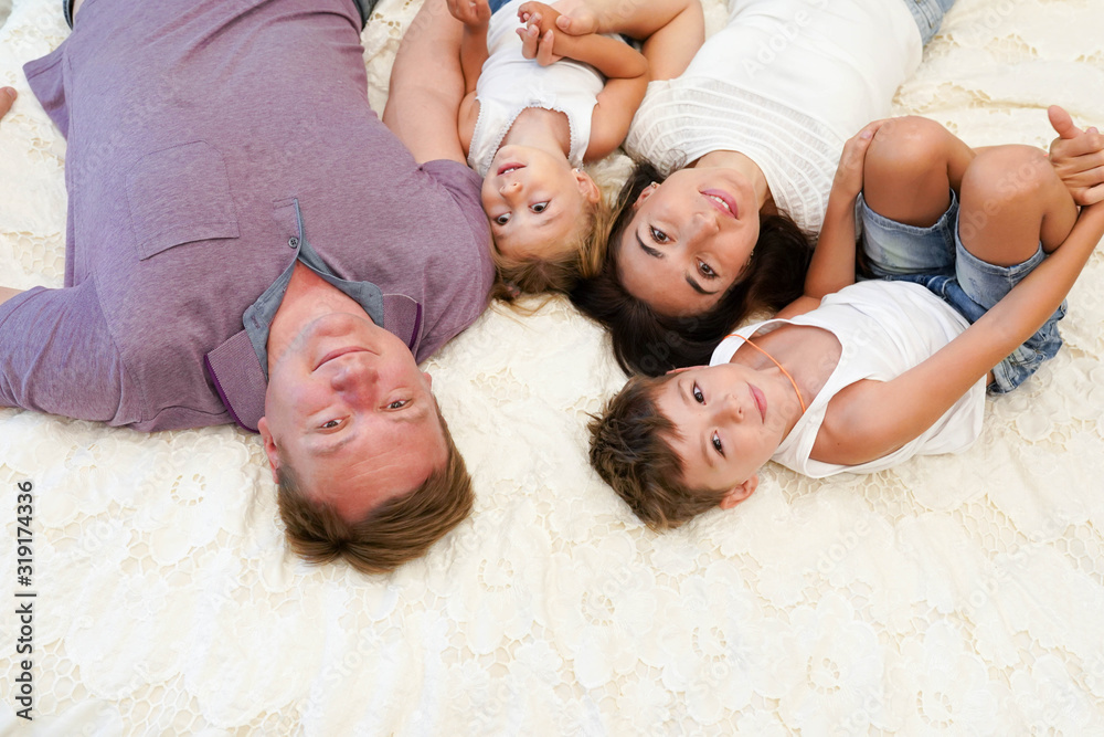 Top view of beautiful young mother, father and their children looking at camera and smiling while lying on bed head to head