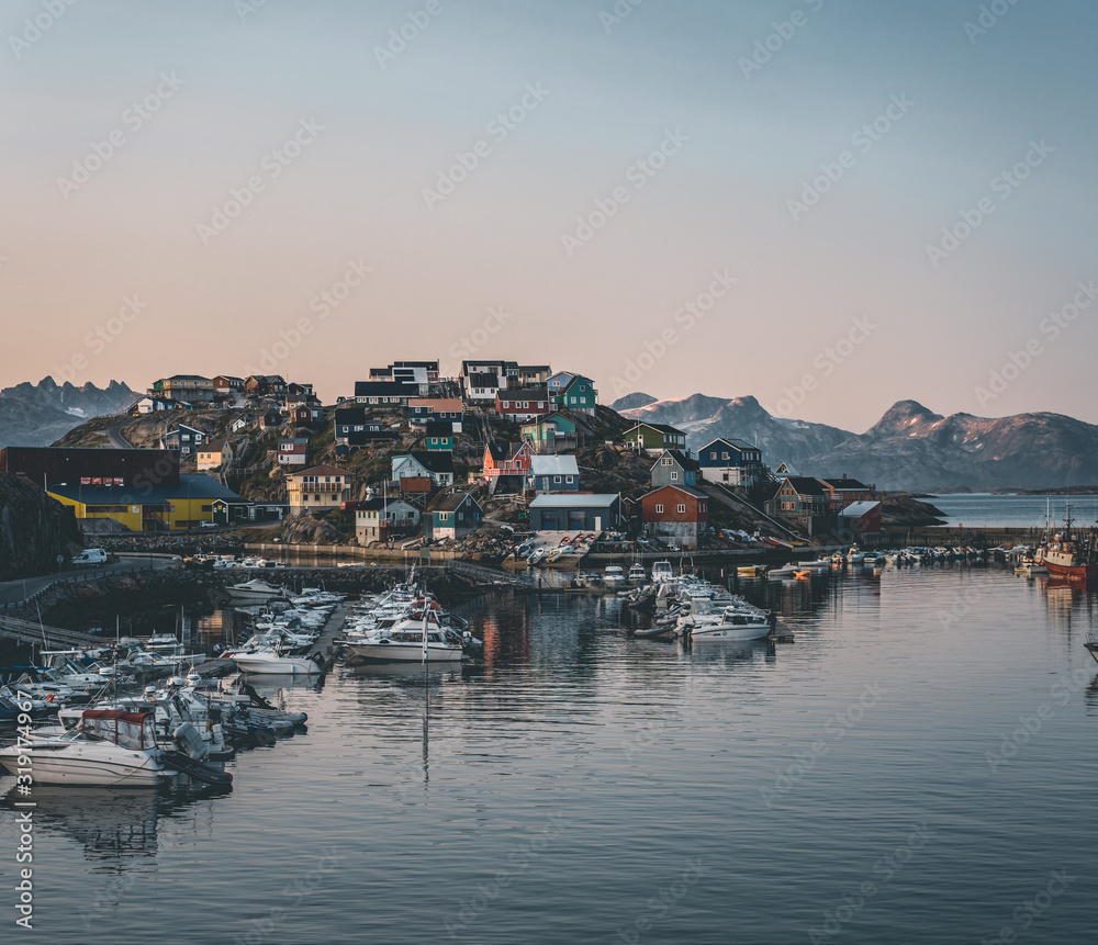 Sunset view of Maniitsoq arctic city in Greenland. Mountains in background during midnight sun. Colourfull houses and panorama. View to port with ships.