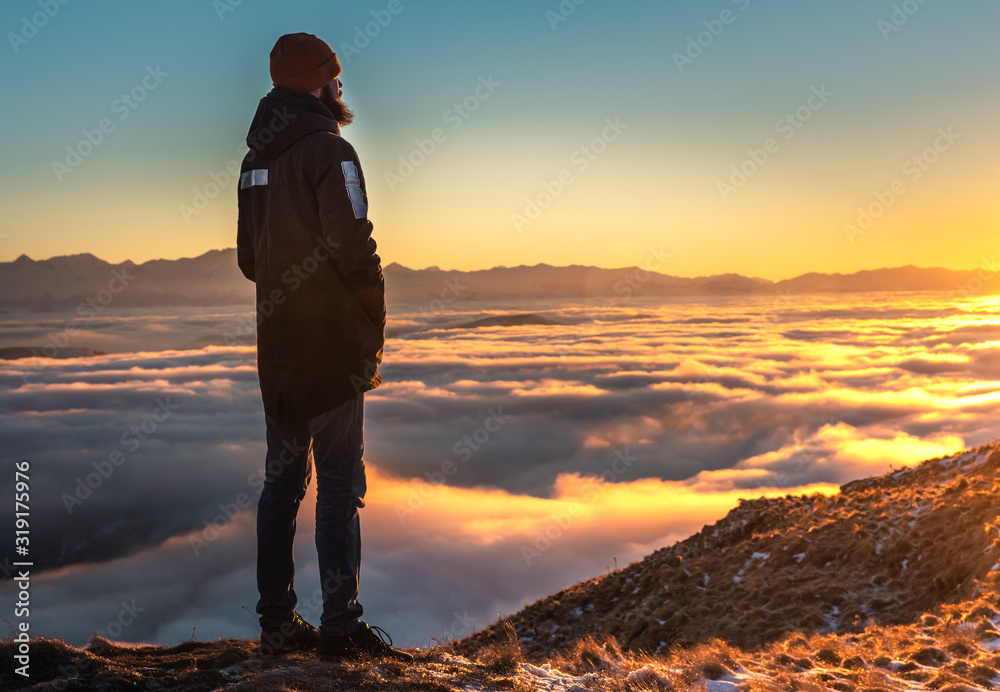 A man stands high in the mountains, at sunset, above the clouds.