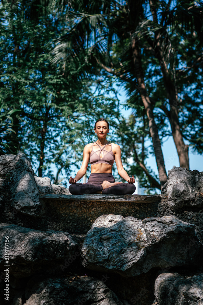 Raising spirit. Full-length shot of caucasian woman sitting in Easy Seated pose, Sukhasana while practicing yoga outdoors, in a garden. Healthy lifestyle and relaxation concept