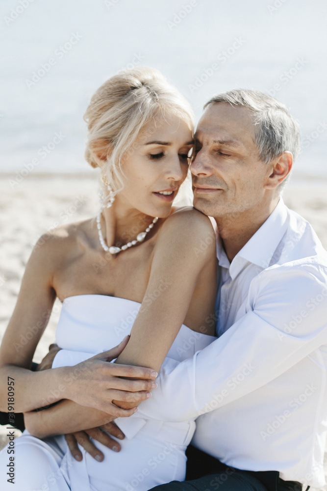 Tender grownup couple near the sea on the beach is hugging in white clothes