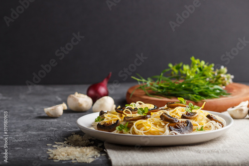 Rice noodles with champignons mushrooms, egg sauce and oregano on a black concrete background. side view, copy space.