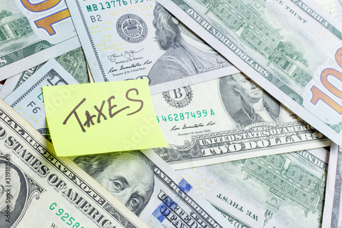 The inscription "taxes" on a yellow memo stick note on us dollar money background