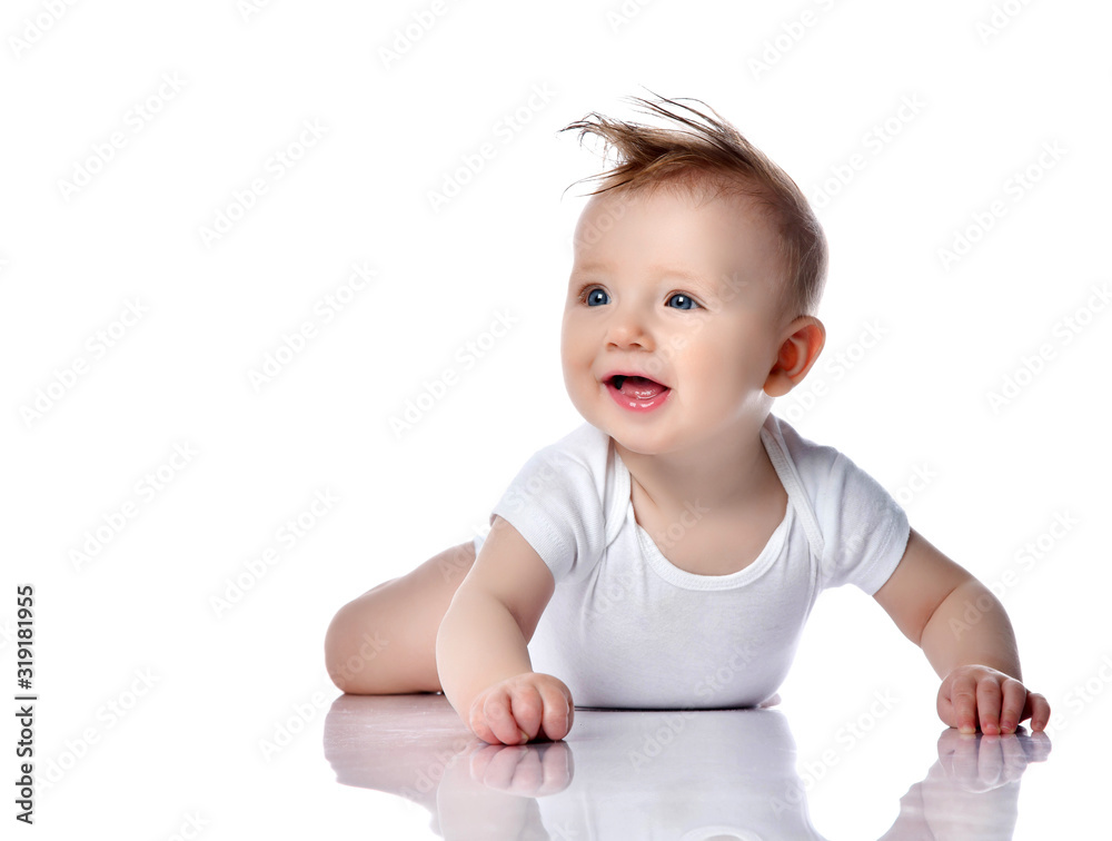 Happy smiling infant child baby boy toddler with blue eyes in white bodysuit lies on the floor on his stomach looking Happy smiling infant child baby boy toddler with blue eyes in white bodysuit lies on the floor on his stomach looking