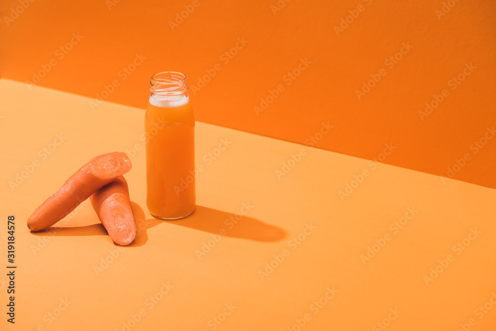 fresh juice in glass bottle near ripe carrots on orange background fresh juice in glass bottle near ripe carrots on orange background