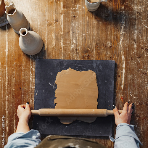 Close up of Wooden Rolling Pin Rolling Out and Flattening Clay on Gray Board For Ceramics Tableware. Top view. photo