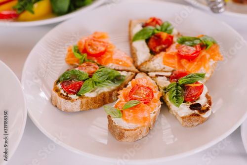 Little stylish sandwiches with red fish and tomatoes. Fish snack for the holiday table. Elegant canapes and salmon.
