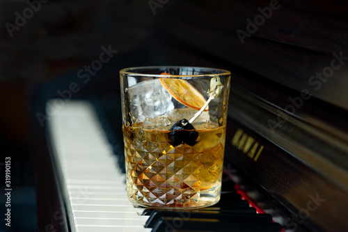 Old fashioned cocktail with orange and cherry on the piano keys.