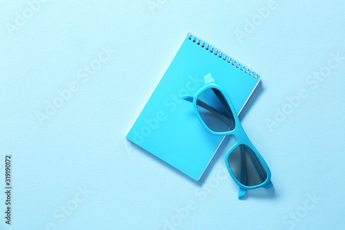 Stylish eyeglasses with notebook on color background
