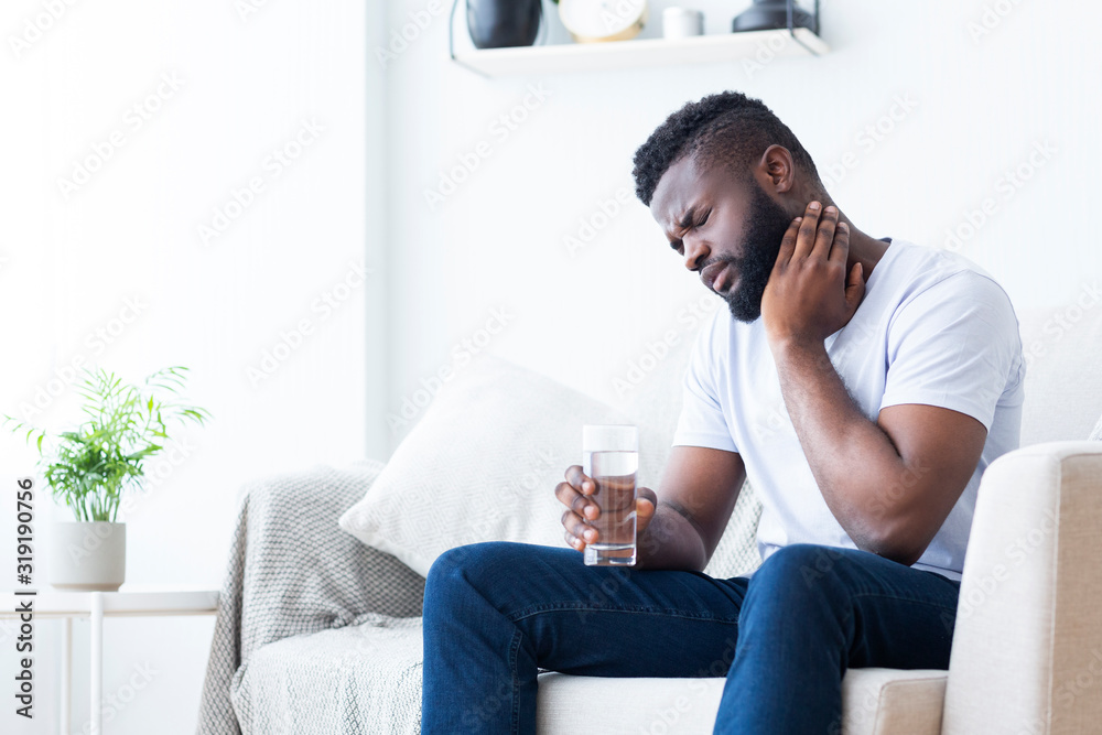 Φωτογραφία Young african man touching his neck and holding glass of water