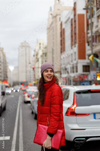Smiling young woman in red coat and a laptop walking downtown © Ignacio Ferrándiz