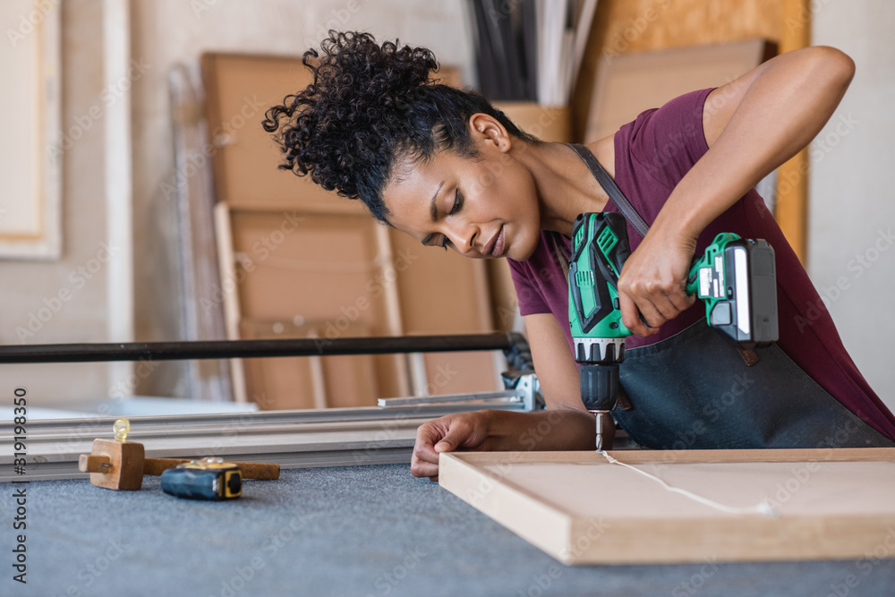 Foto Woman assembling a frame with a drill in her workshop