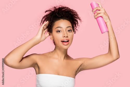 attractive african american girl with bottle of hair spray, isolated on pink
