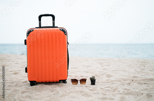 Summer holiday and traveling concept with orange suitcase and sunglasses is on the beach and seaside with copy space