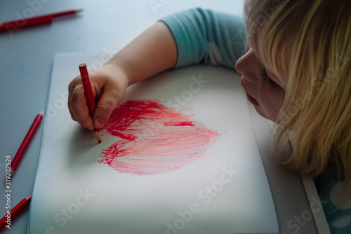 Foto Little girl drawing red heart at white paper within red pens and pencils