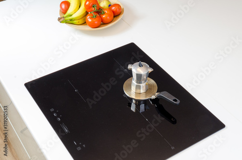  induction cooker with an adapter, coffee tea pot mokka coffee maker, modern glass kitchen stove top, low energy consumption and high efficiency, black glass on white kitchen worktop, fruit on te plat