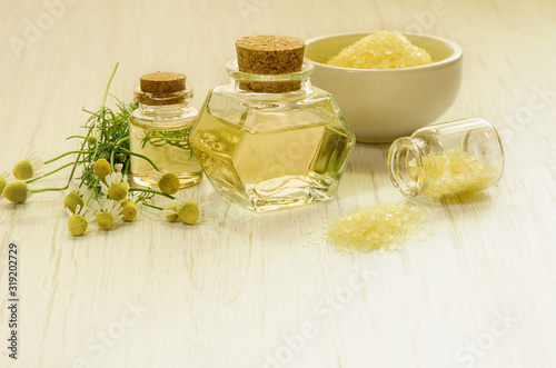 Yellow chamomile water or extract in glass bottles, Spa salt and fresh flower with leaves on wooden white background