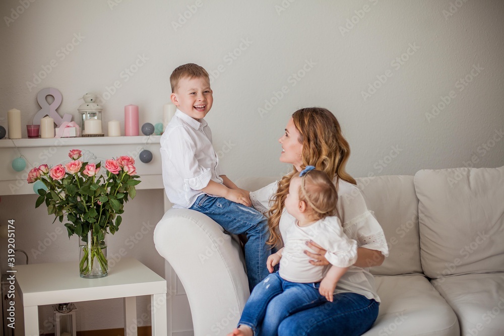 Beautiful young mother, little son, little daughter are sitting on the sofa at home. Mothers Day. A happy family. Cozy. Beautiful young mother, little son, little daughter are sitting on the sofa at home. Mothers Day. A happy family. Cozy.