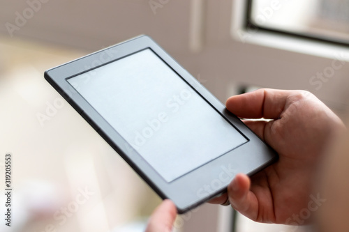 Male hands with modern e-book with blank screen closeup. Reading at home on the balcony with a pocket reader