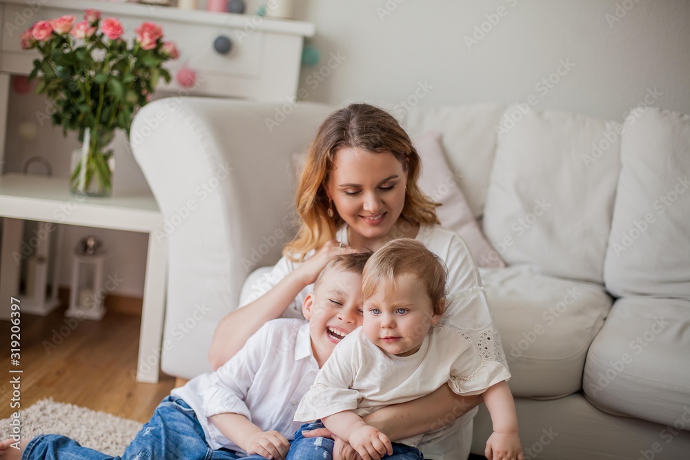 Beautiful young mother, little son, little daughter are sitting on the sofa at home. Mothers Day. A happy family. Cozy. Beautiful young mother, little son, little daughter are sitting on the sofa at home. Mothers Day. A happy family. Cozy.