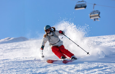 Girl On the Ski. a skier in a bright suit and outfit with long pigtails on her head rides on the track with swirls of fresh snow. Active winter holidays, skiing downhill in sunny day. Woman skier