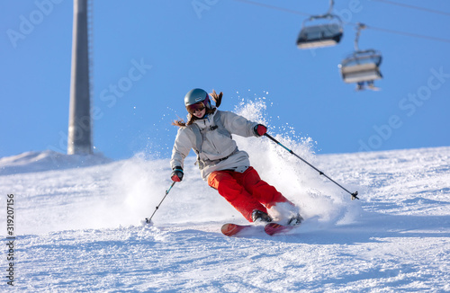 Girl On the Ski. a skier in a bright suit and outfit with long pigtails on her head rides on the track with swirls of fresh snow. Active winter holidays, skiing downhill in sunny day. Woman skier photo