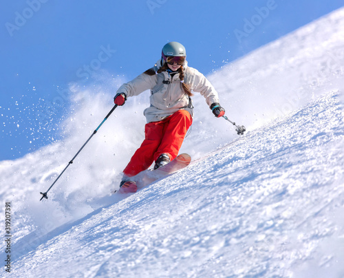 Girl On the Ski. a skier in a bright suit and outfit with long pigtails on her head rides on the track with swirls of fresh snow. Active winter holidays, skiing downhill in sunny day. Woman skier