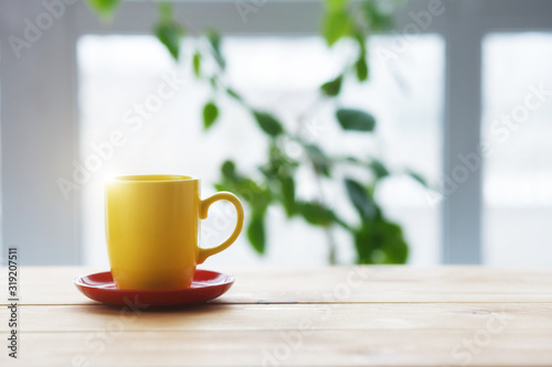 yellow coffee cup on wooden table, blurred nature background, copy space, morning sunlight