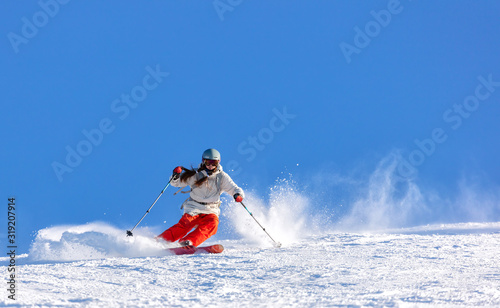 Girl On the Ski. a skier in a bright suit and outfit with long pigtails on her head rides on the track with swirls of fresh snow. Active winter holidays, skiing downhill in sunny day. Woman skier