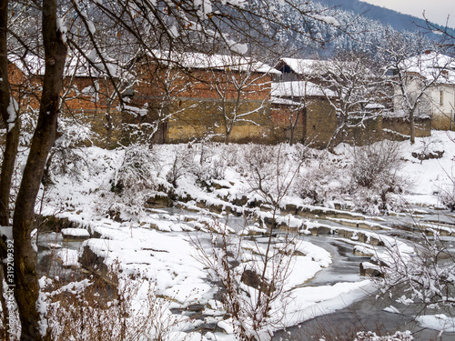 Picturesque snowy rural view of the frozen Vidima River and riverbank houses at the Bulgarian Fore-Balkan village of Debnevo, Central-North Bulgaria photo