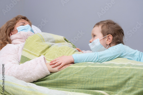 A woman and a child lie on a bed in medical masks. Virus, mom is sick and daughter condoles. Europeans and Coronavirus photo