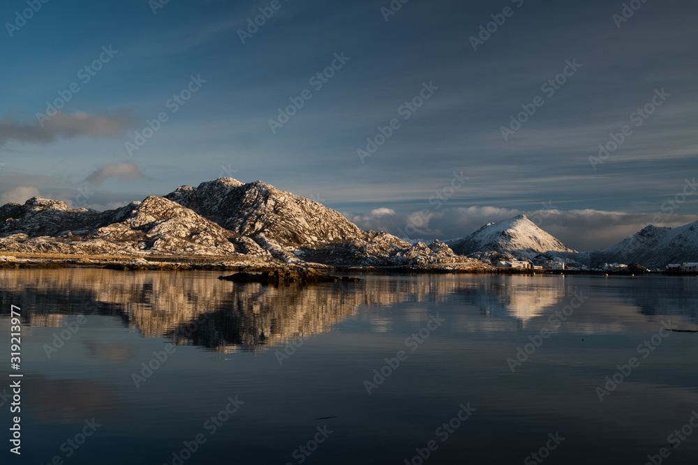 Sunrise in small town Ballstad located in Lofoten islands. Sun is lightening hills. Reflection in the sea. Beautiful morning in northern paradise.