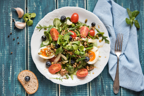 Salad of arugula, tomatoes, nuts and eggs. View from above. Wooden table. Place for text.