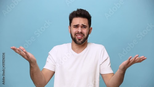 Handsome unshaven bearded young guy 20s in white t-shirt isolated on pastel blue background in studio. People sincere emotions lifestyle concept. Looking at camera expressive gesticulating with hands photo