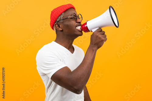 stylish black handsome smiling american man in white t-shirt speaks news through a megaphone on isolated orange background with copy space