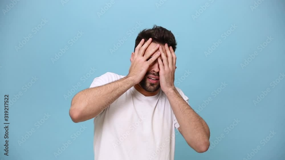 Unshaven bearded young guy 20s wearing white t-shirt isolated over pastel blue background in studio. People sincere emotions lifestyle concept. Looking at camera cover face with hands scared shocked Unshaven bearded young guy 20s wearing white t-shirt isolated over pastel blue background in studio. People sincere emotions lifestyle concept. Looking at camera cover face with hands scared shocked