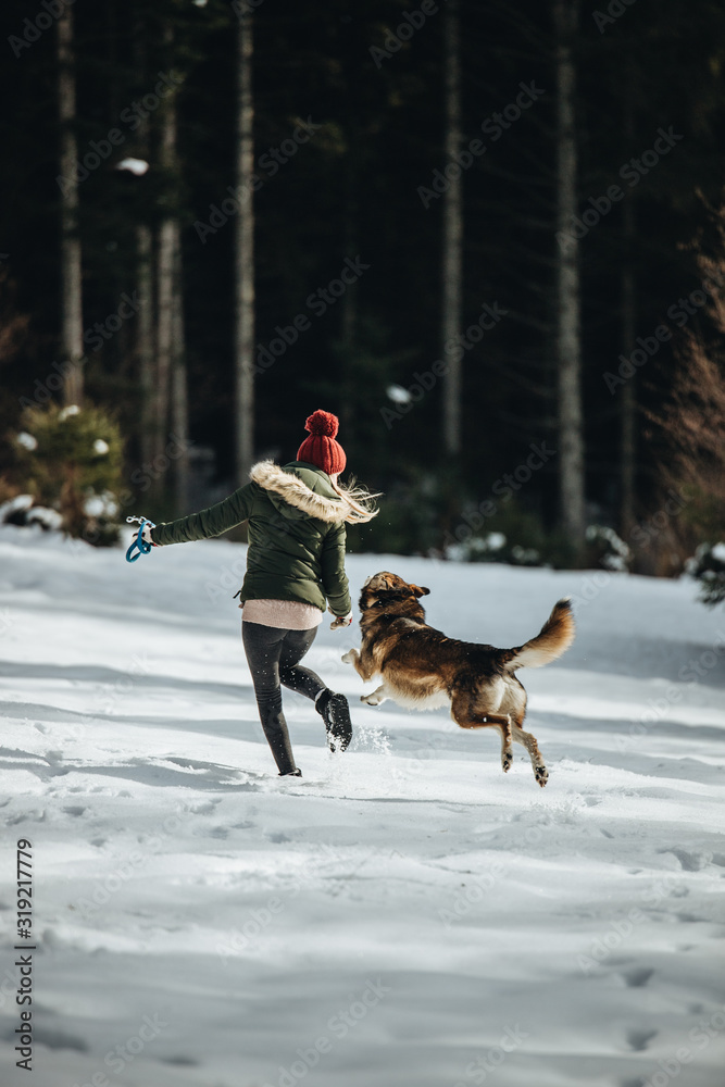 Young happy female and her dog in having fun in fores in winter season.